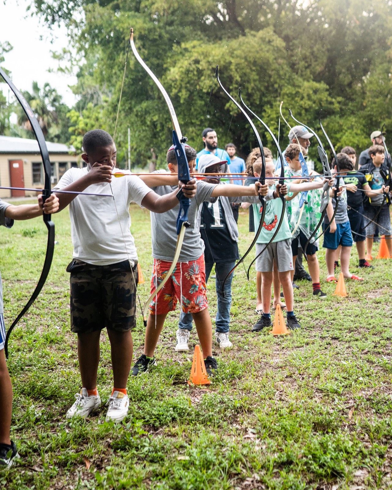 Line of campers practicing archery in an open field at CKids Gan Israel FL